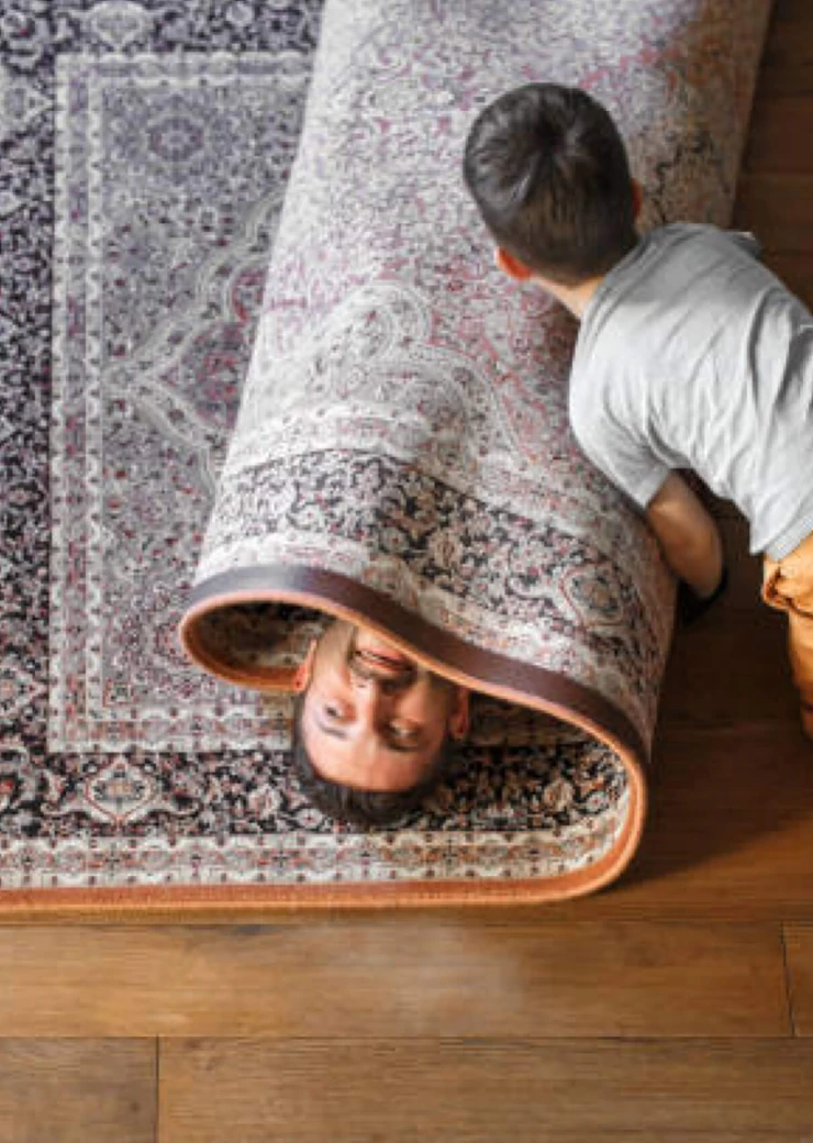 child rolling father up in a carpet playing on hardwood floors Buddy's Flooring America 